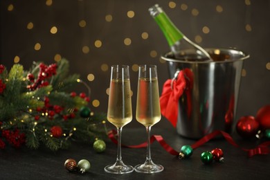 Photo of Delicious champagne in glasses and Christmas decor on grey table against blurred lights