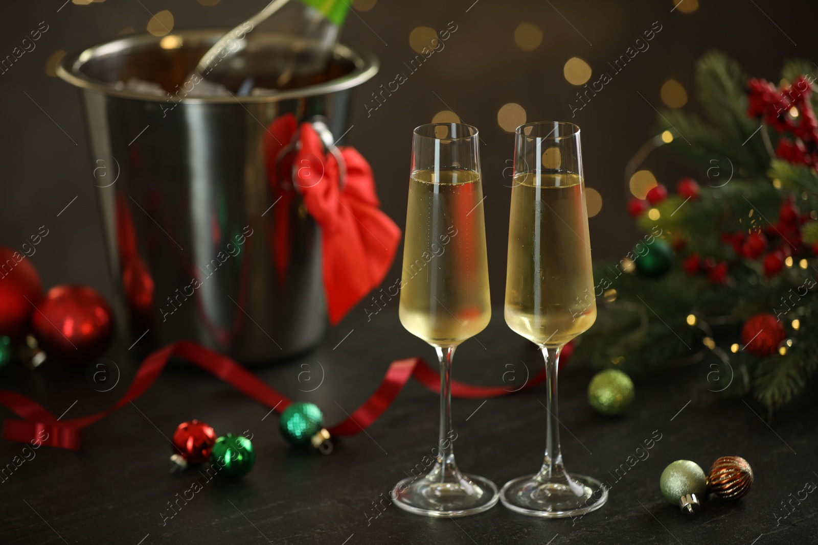 Photo of Delicious champagne in glasses and Christmas decor on grey table against blurred lights, space for text