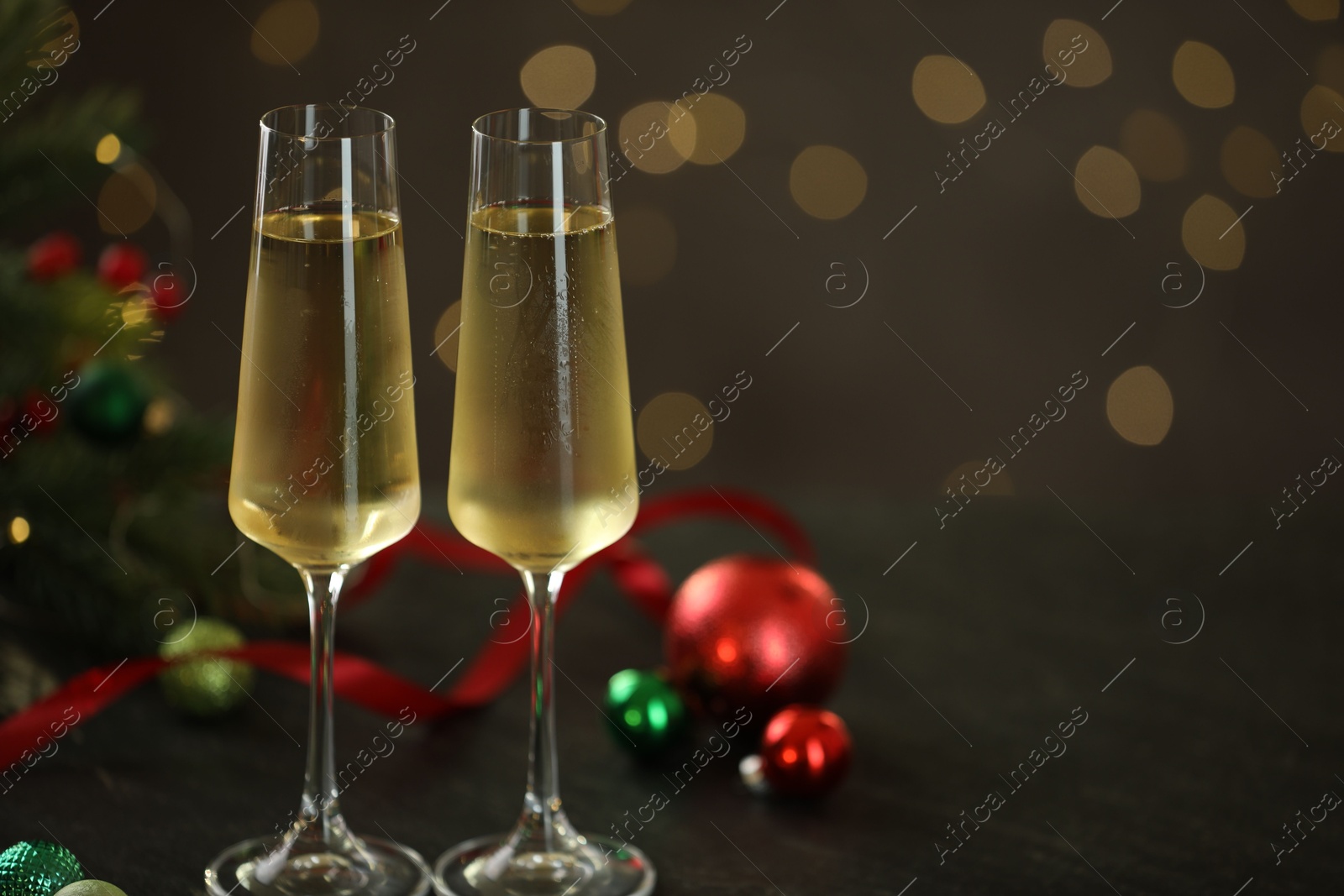 Photo of Delicious champagne in glasses and Christmas decor on grey table against blurred lights, space for text