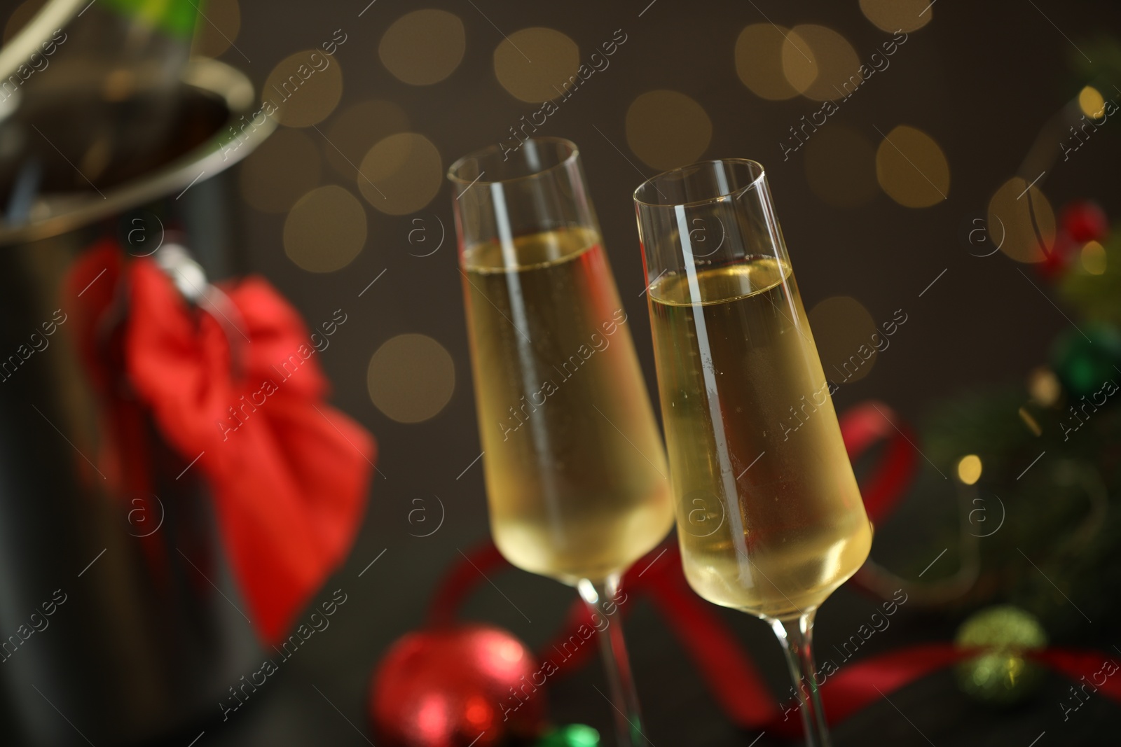 Photo of Delicious champagne in glasses and Christmas decor against grey background with blurred lights, closeup