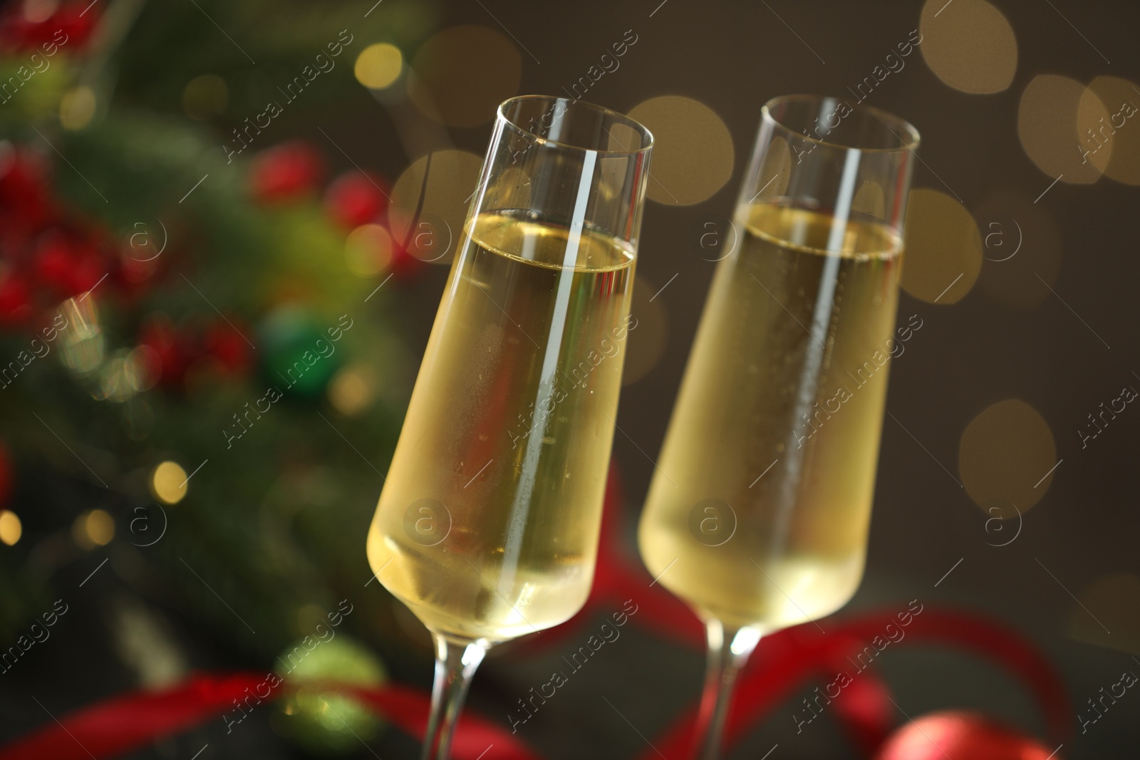 Photo of Delicious champagne in glasses and Christmas decor against grey background with blurred lights, closeup