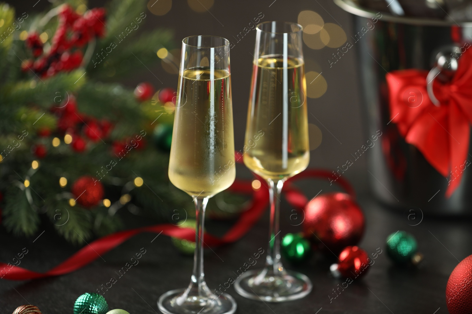 Photo of Delicious champagne in glasses and Christmas decor on grey table against blurred lights