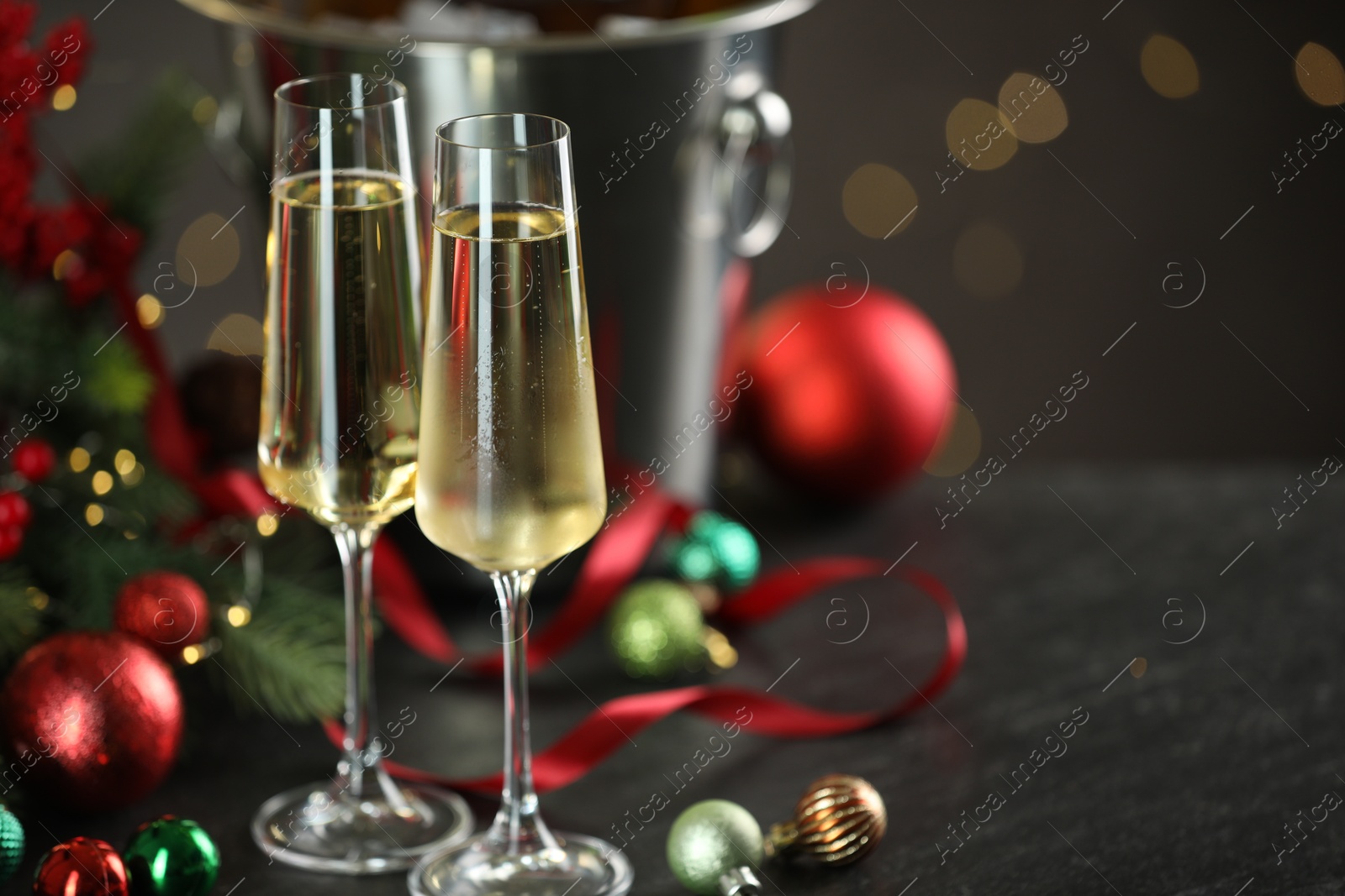 Photo of Delicious champagne in glasses and Christmas decor on grey table against blurred lights, space for text