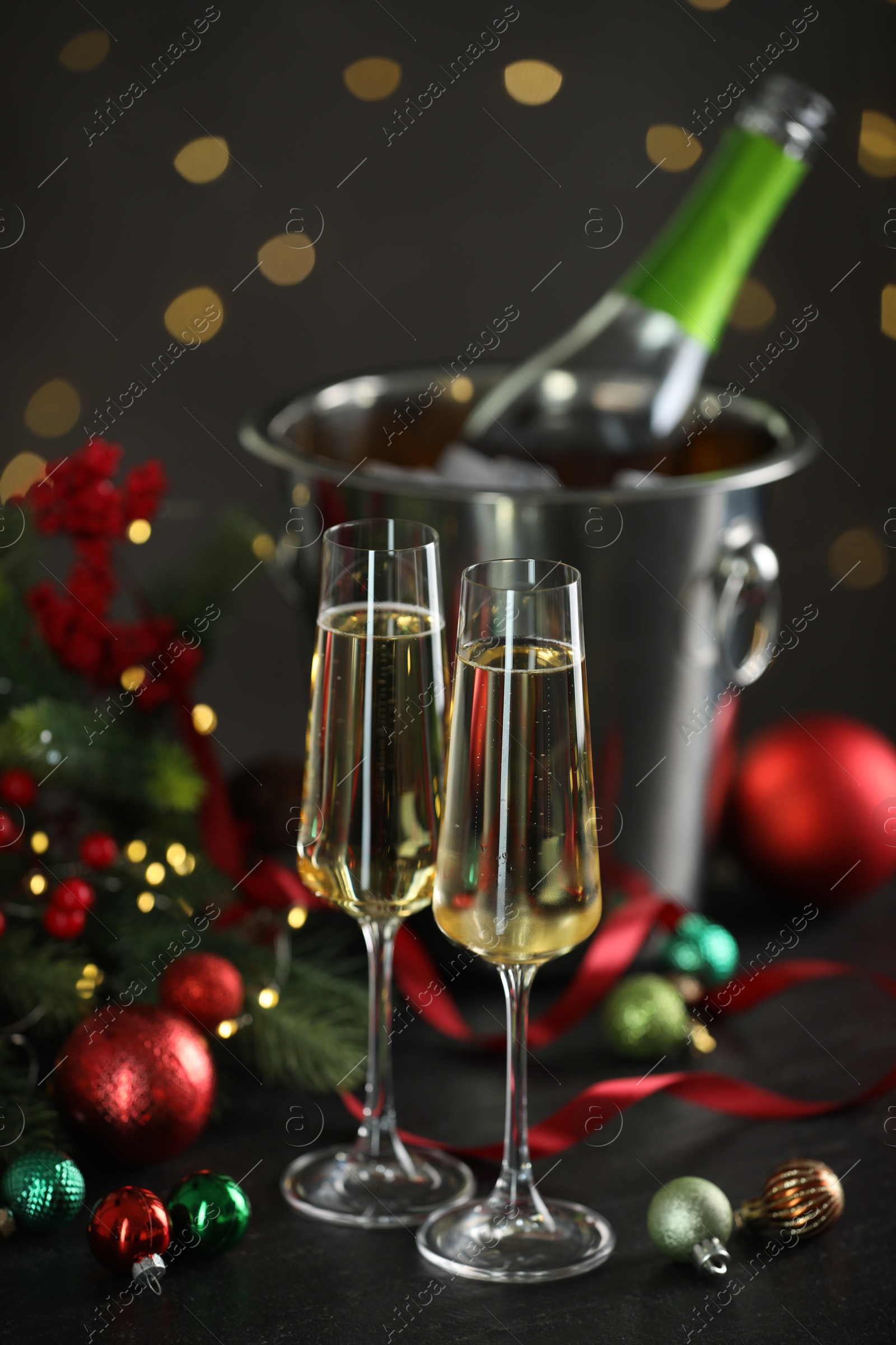 Photo of Delicious champagne in glasses and Christmas decor on grey table against blurred lights