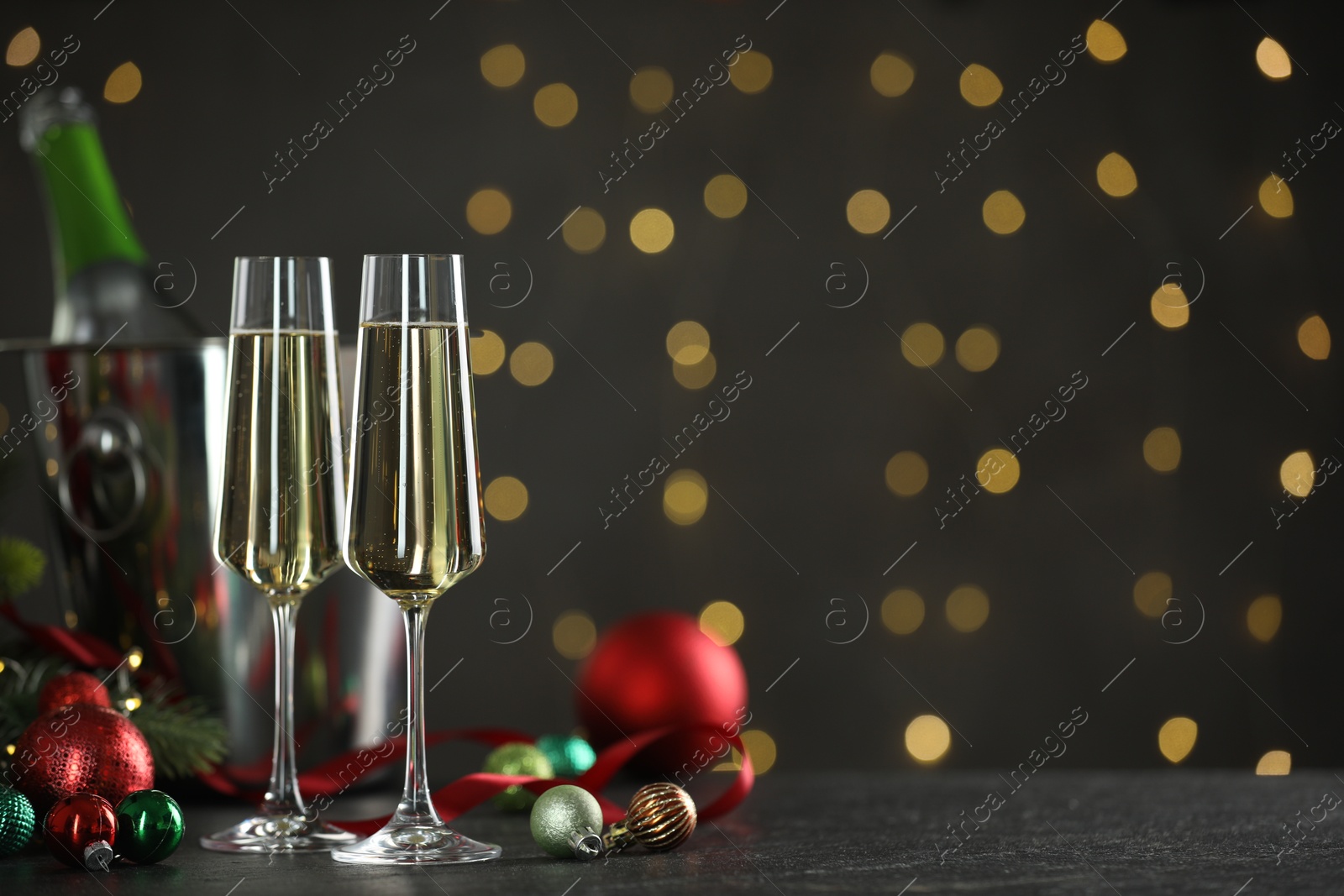 Photo of Delicious champagne in glasses and Christmas decor on grey table against blurred lights, space for text