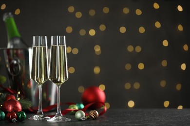 Photo of Delicious champagne in glasses and Christmas decor on grey table against blurred lights, space for text