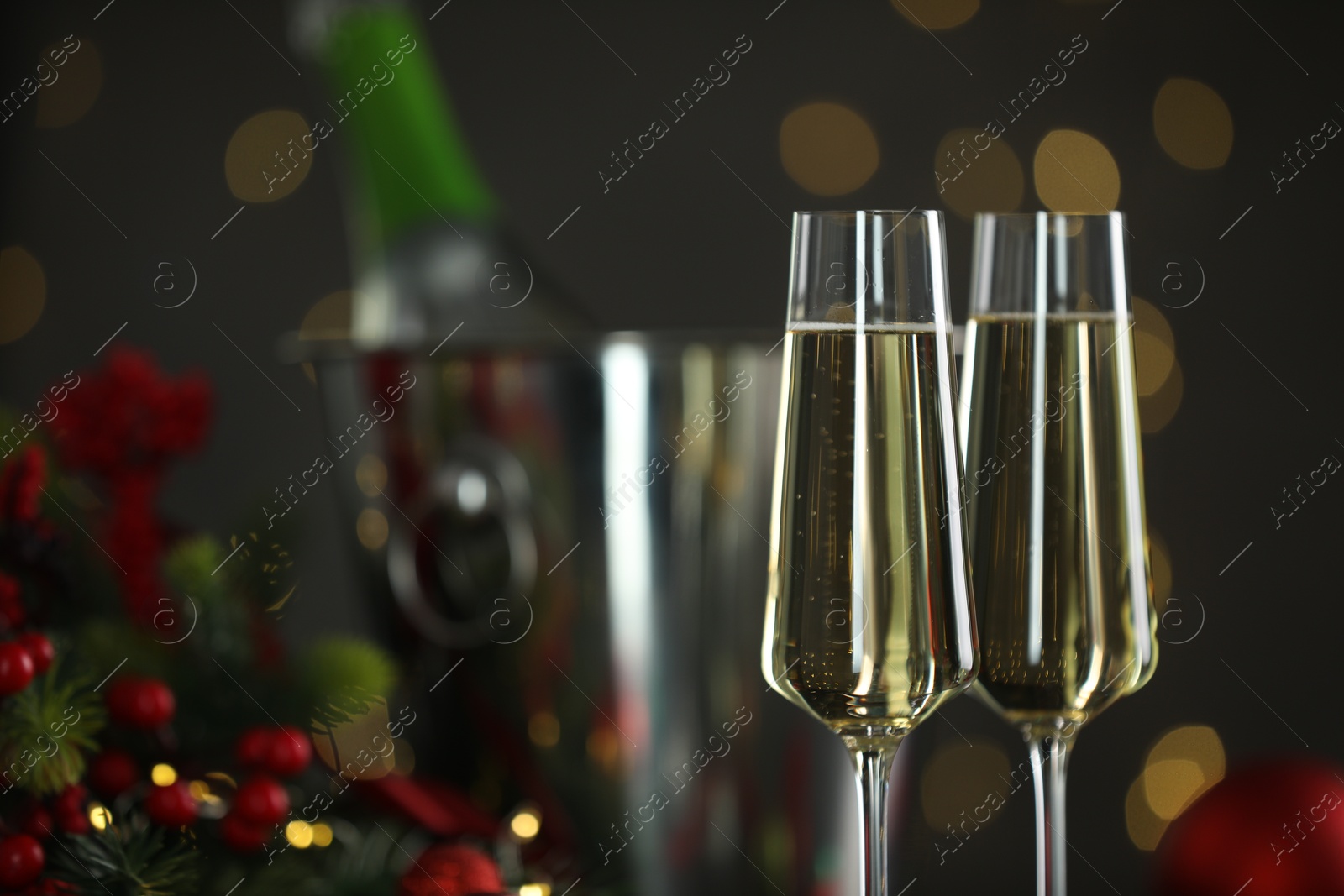 Photo of Delicious champagne in glasses and Christmas decor against grey background with blurred lights, closeup. Space for text