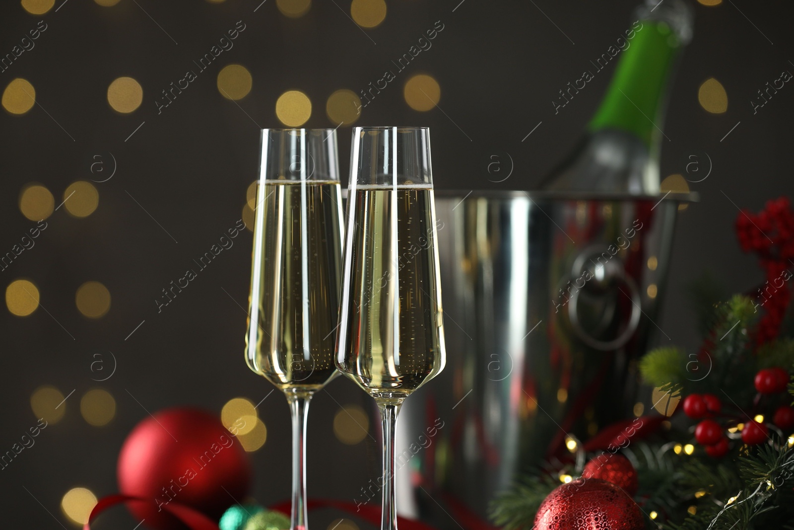 Photo of Delicious champagne in glasses and Christmas decor against grey background with blurred lights, closeup