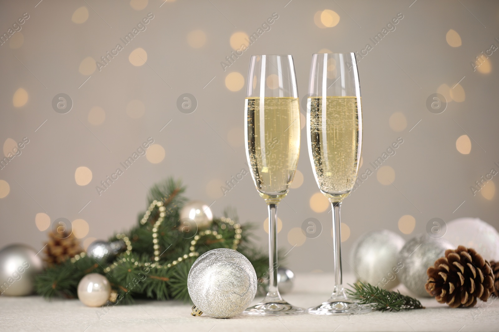 Photo of Delicious champagne in glasses and Christmas decor on white table against blurred lights