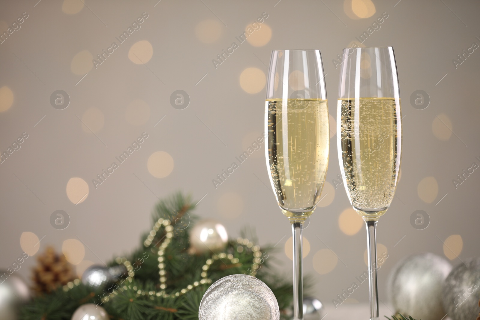 Photo of Delicious champagne in glasses and Christmas decor against light grey background with blurred lights, closeup. Space for text