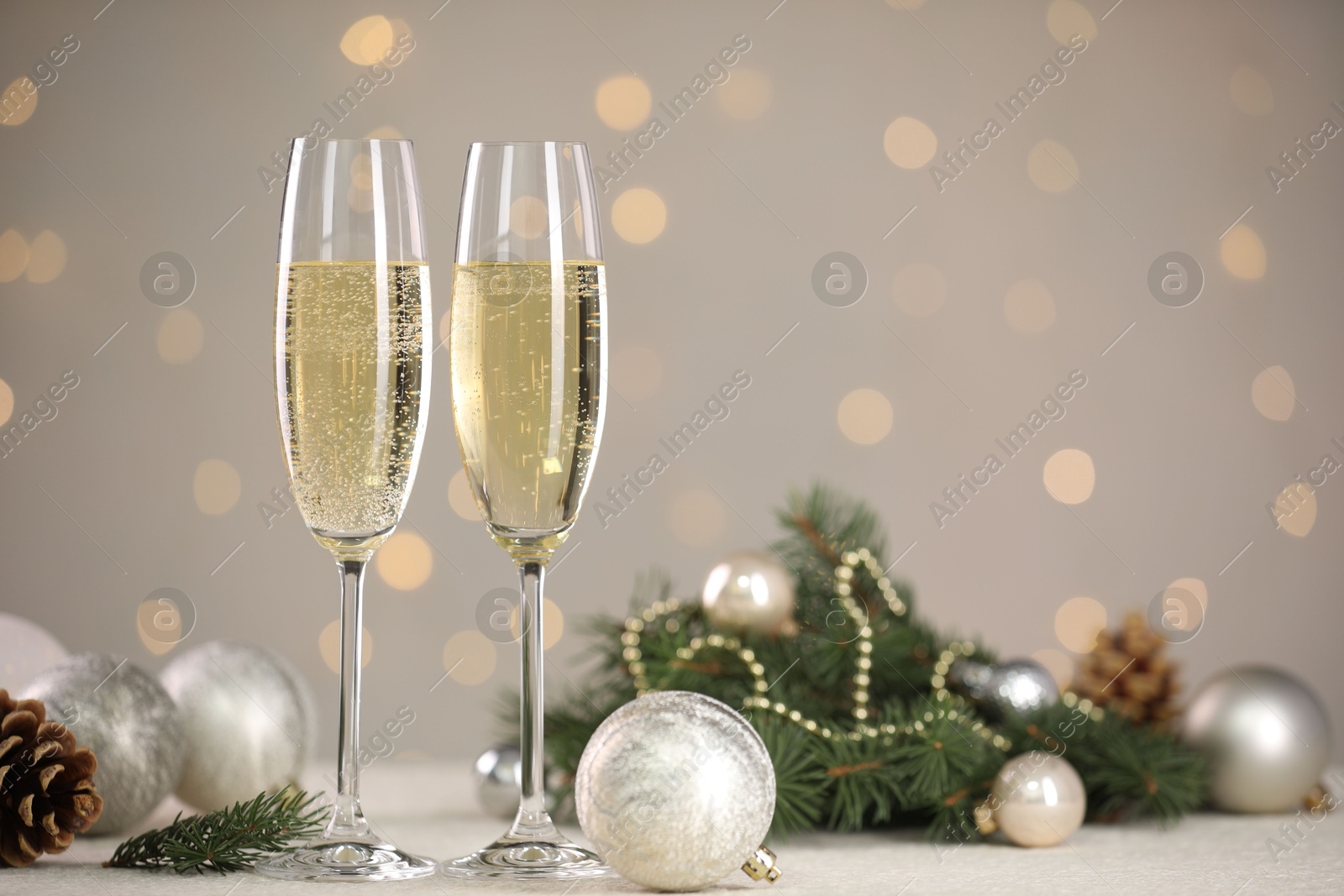 Photo of Delicious champagne in glasses and Christmas decor on white table against blurred lights, space for text