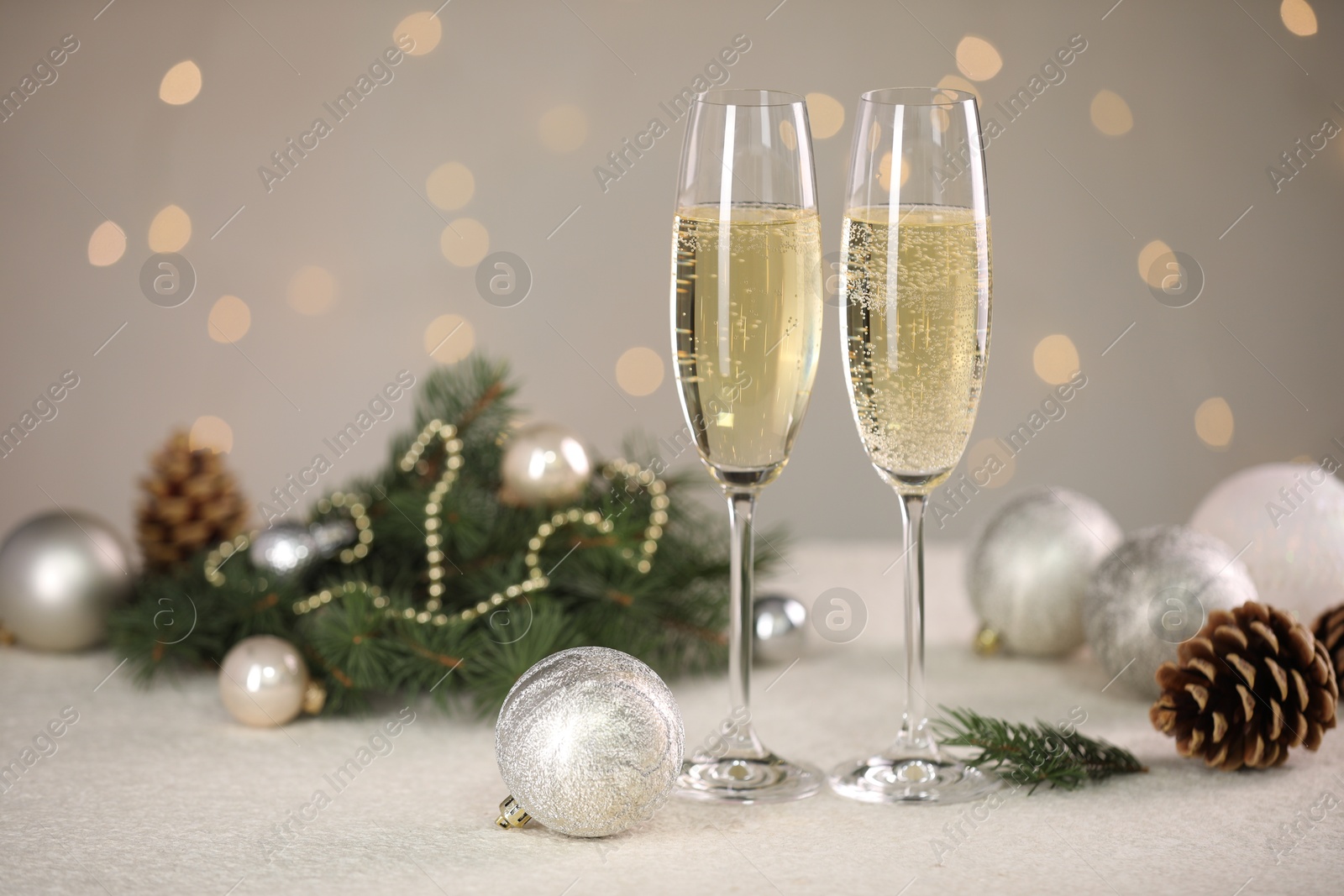 Photo of Delicious champagne in glasses and Christmas decor on white table against blurred lights, space for text