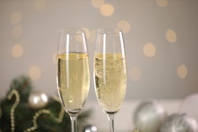 Delicious champagne in glasses and Christmas decor against light grey background with blurred lights, closeup