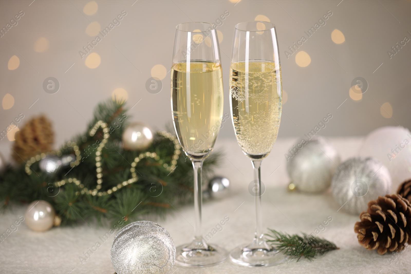 Photo of Delicious champagne in glasses and Christmas decor on white table against blurred lights