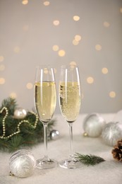 Photo of Delicious champagne in glasses and Christmas decor on white table against blurred lights