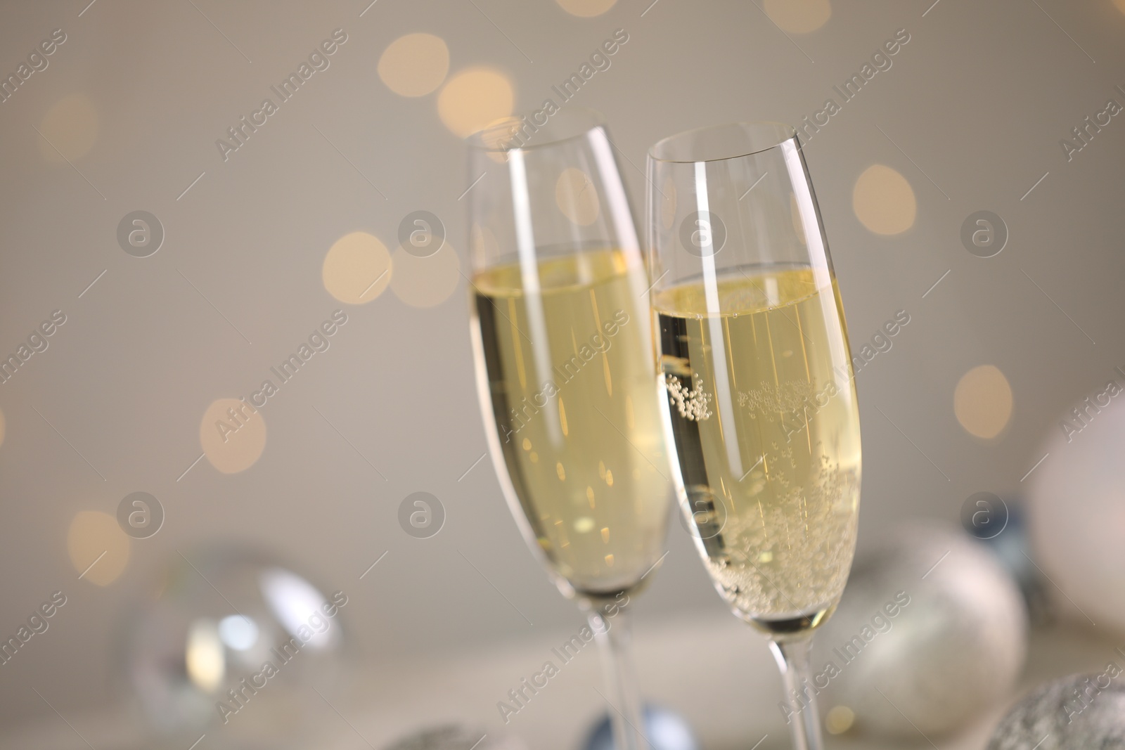 Photo of Delicious champagne in glasses and Christmas decor against light grey background with blurred lights, closeup