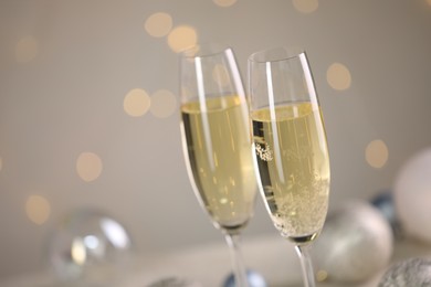 Photo of Delicious champagne in glasses and Christmas decor against light grey background with blurred lights, closeup