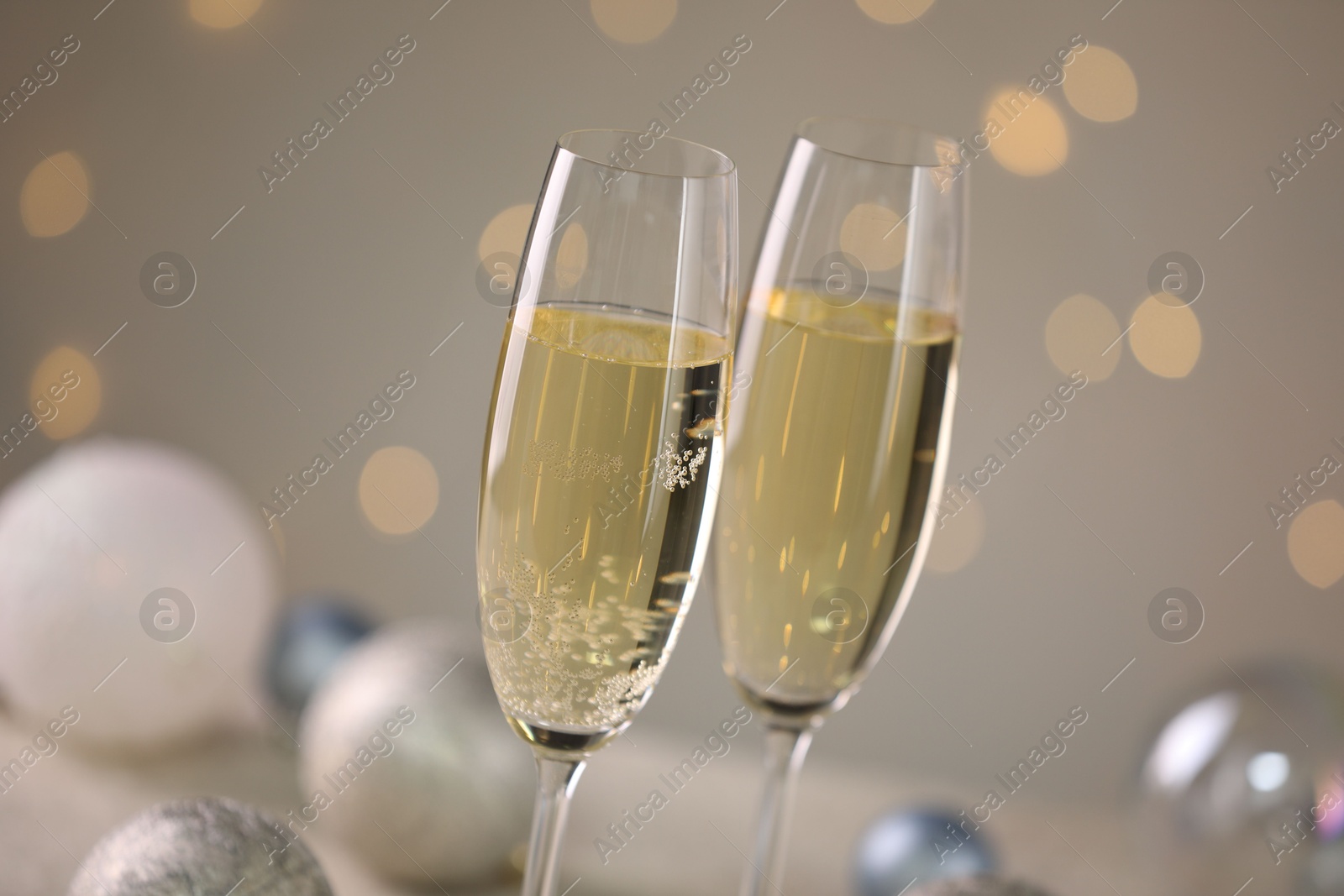 Photo of Delicious champagne in glasses and Christmas decor against light grey background with blurred lights, closeup