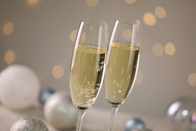 Photo of Delicious champagne in glasses and Christmas decor against light grey background with blurred lights, closeup