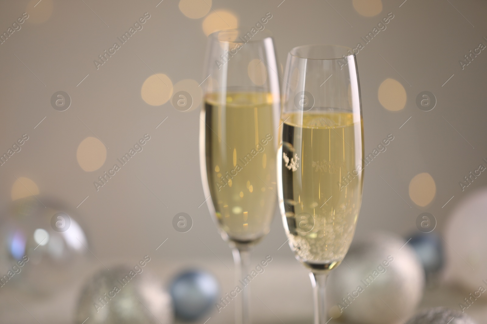 Photo of Delicious champagne in glasses and Christmas decor against light grey background with blurred lights, closeup