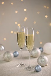 Photo of Delicious champagne in glasses and Christmas decor on white table against blurred lights