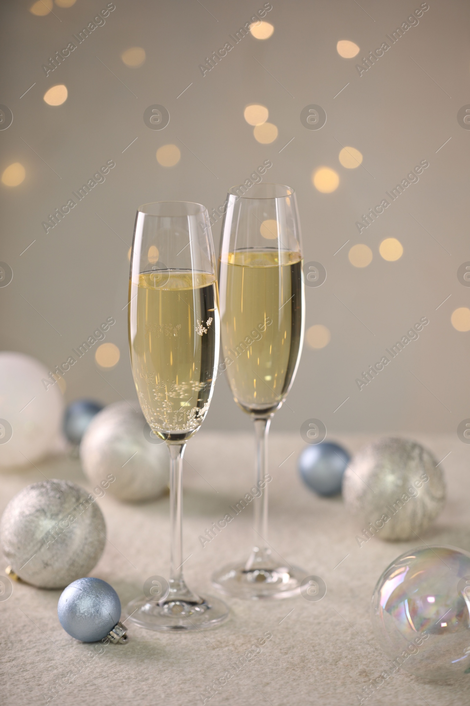 Photo of Delicious champagne in glasses and Christmas decor on white table against blurred lights