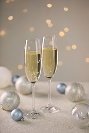 Photo of Delicious champagne in glasses and Christmas decor on white table against blurred lights