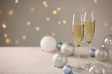 Photo of Delicious champagne in glasses and Christmas decor on white table against blurred lights, space for text