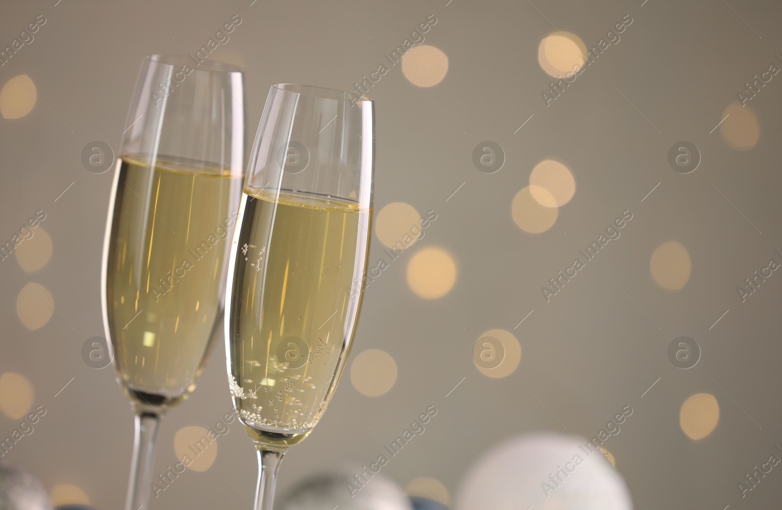 Photo of Delicious champagne in glasses and Christmas decor against light grey background with blurred lights, closeup. Space for text