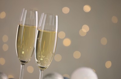 Photo of Delicious champagne in glasses and Christmas decor against light grey background with blurred lights, closeup. Space for text