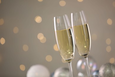 Photo of Delicious champagne in glasses and Christmas decor against light grey background with blurred lights, closeup. Space for text