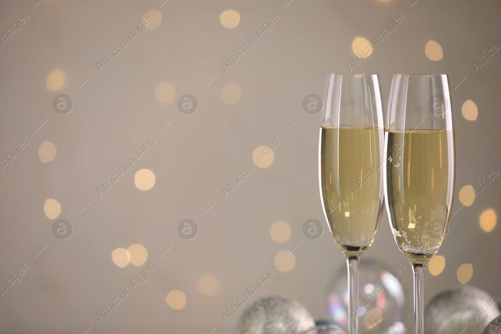 Photo of Delicious champagne in glasses and Christmas decor against light grey background with blurred lights, closeup. Space for text