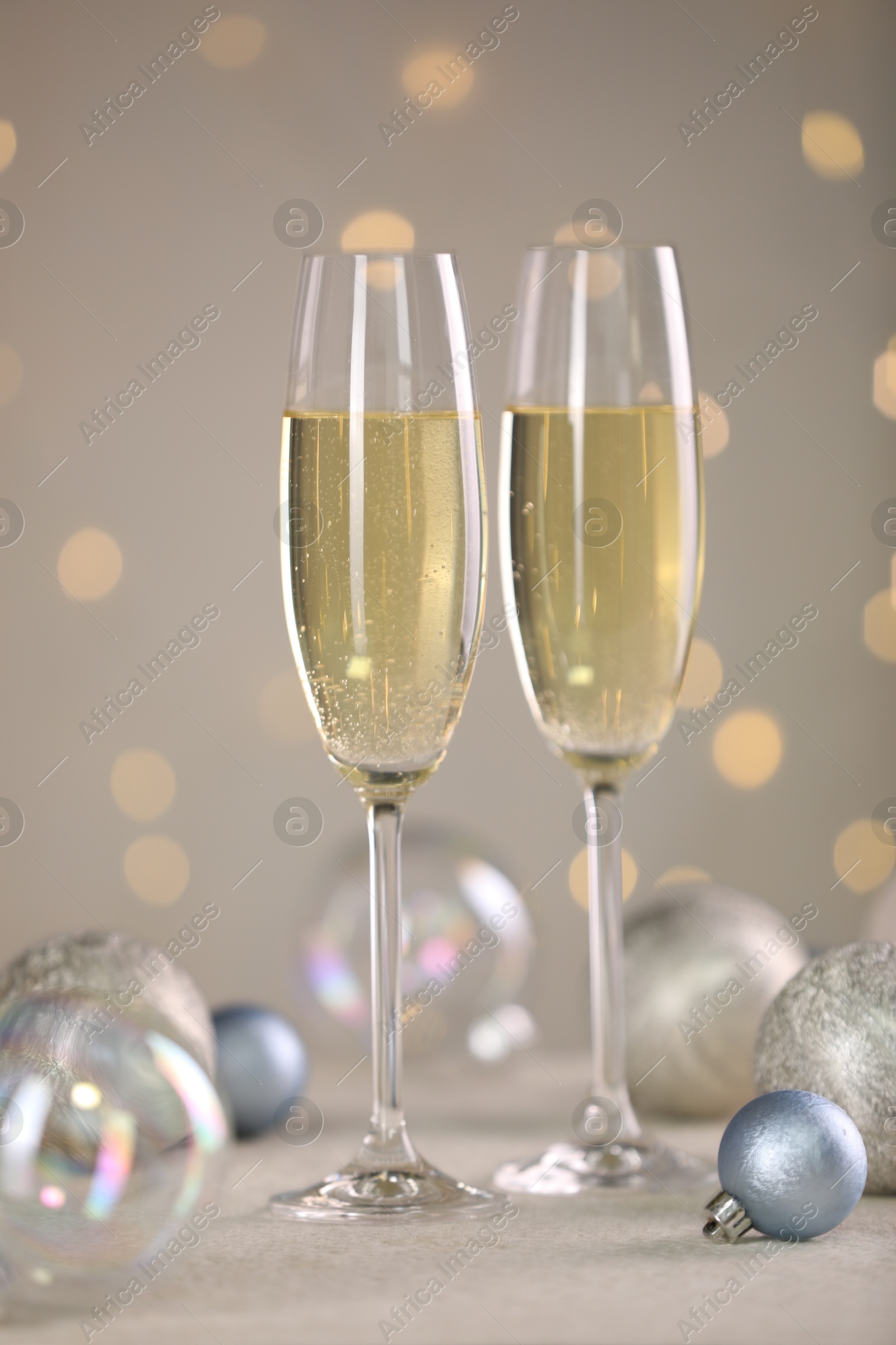 Photo of Delicious champagne in glasses and Christmas decor on white table against blurred lights