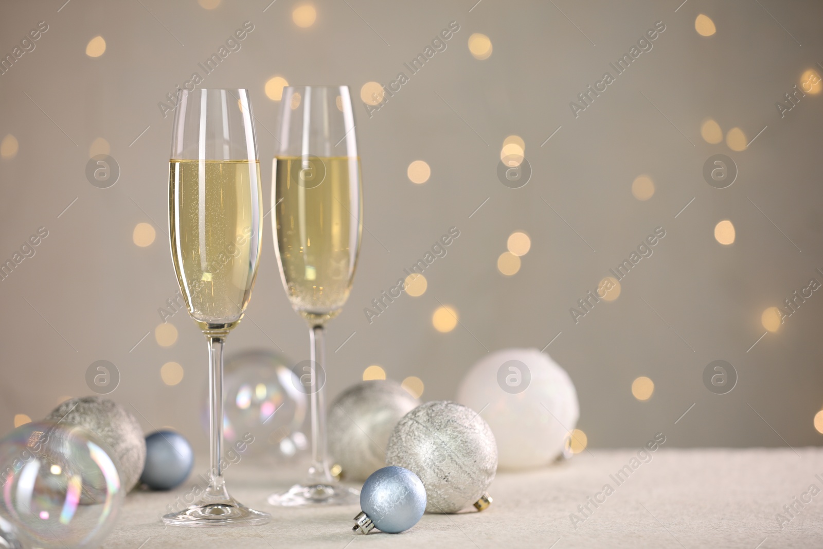 Photo of Delicious champagne in glasses and Christmas decor on white table against blurred lights, space for text