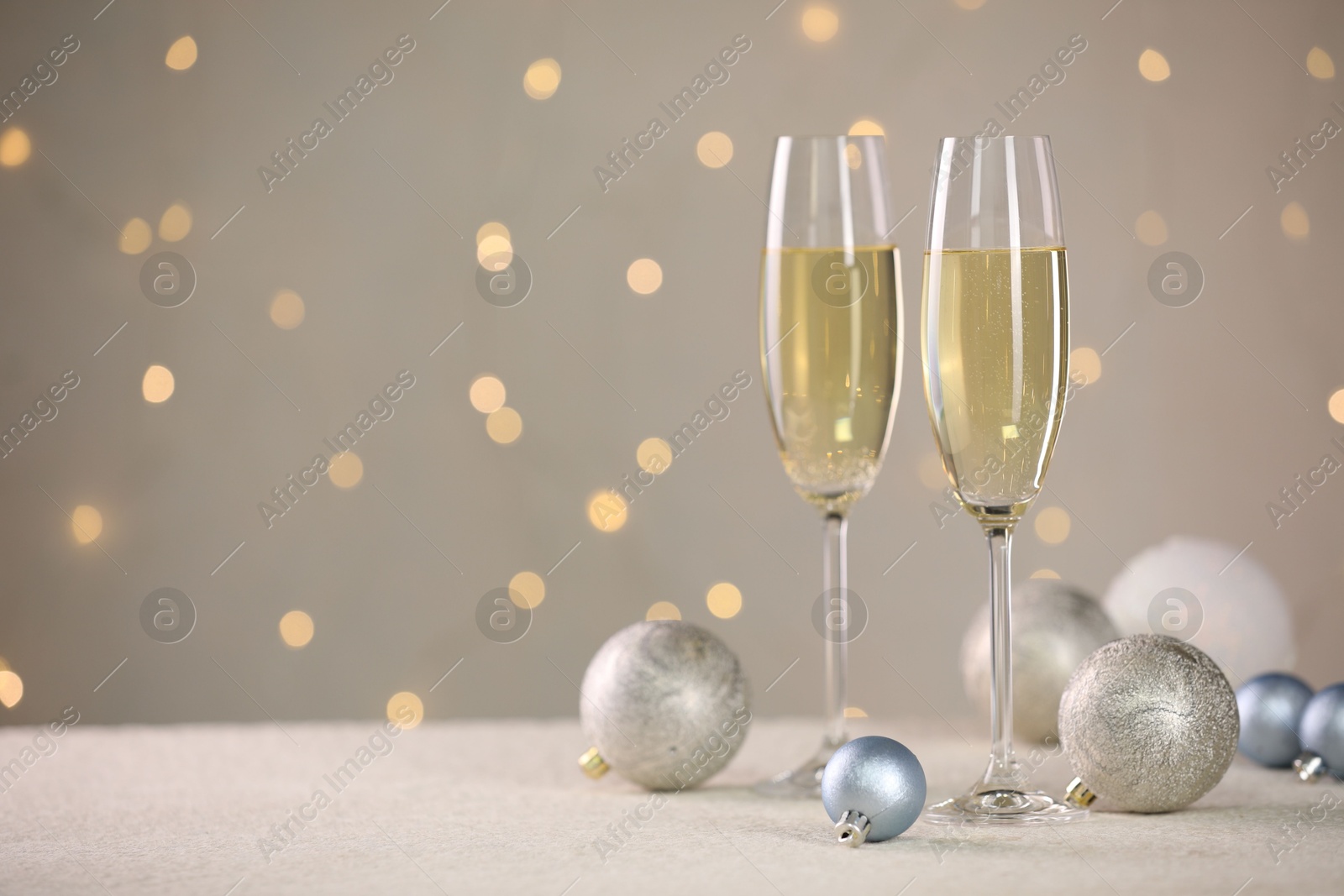 Photo of Delicious champagne in glasses and Christmas decor on white table against blurred lights, space for text