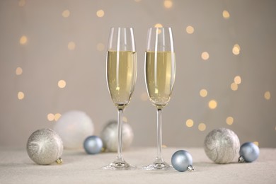 Photo of Delicious champagne in glasses and Christmas decor on white table against blurred lights