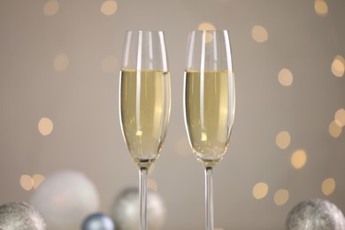 Photo of Delicious champagne in glasses and Christmas decor against light grey background with blurred lights, closeup