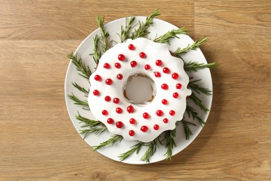 Photo of Traditional Christmas cake decorated with red currants and rosemary on wooden table, top view