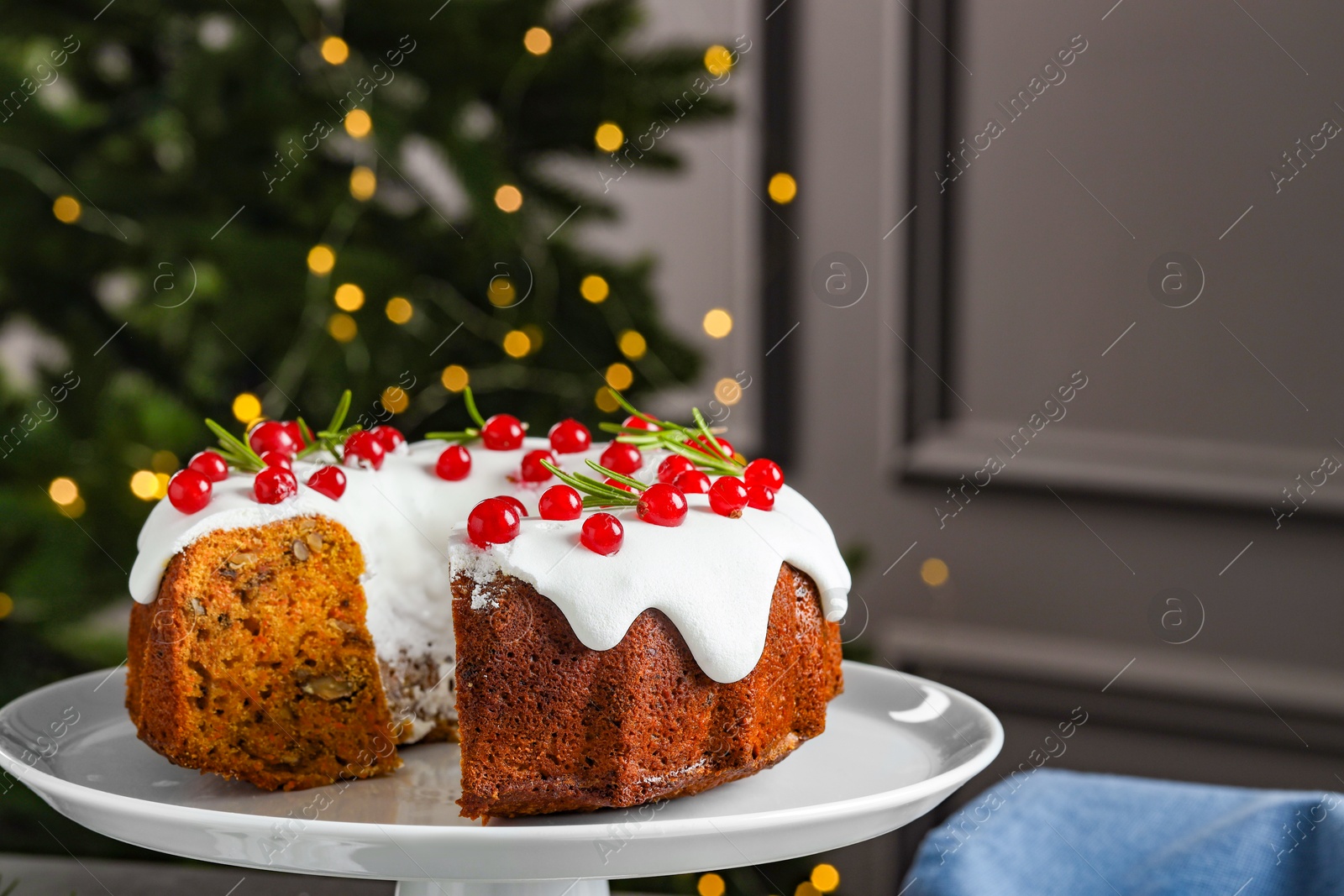 Photo of Traditional Christmas cake decorated with red currants and rosemary on table against blurred lights