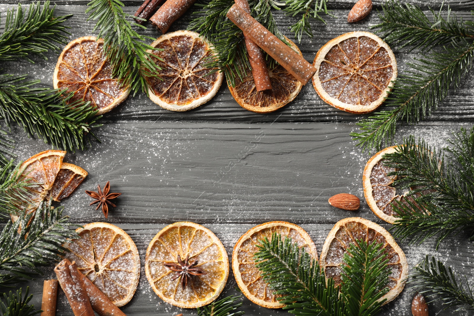 Photo of Frame of different aromatic spices and fir tree branches on grey wooden table, flat lay with space for text. Christmas season