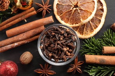 Photo of Different aromatic spices and fir tree branches on black table, flat lay. Christmas season