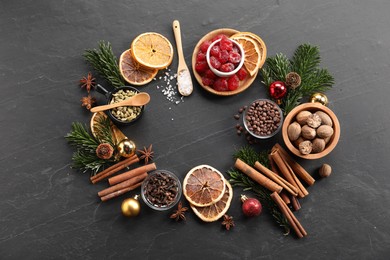 Photo of Frame of different aromatic spices and fir tree branches on black table, flat lay. Christmas season