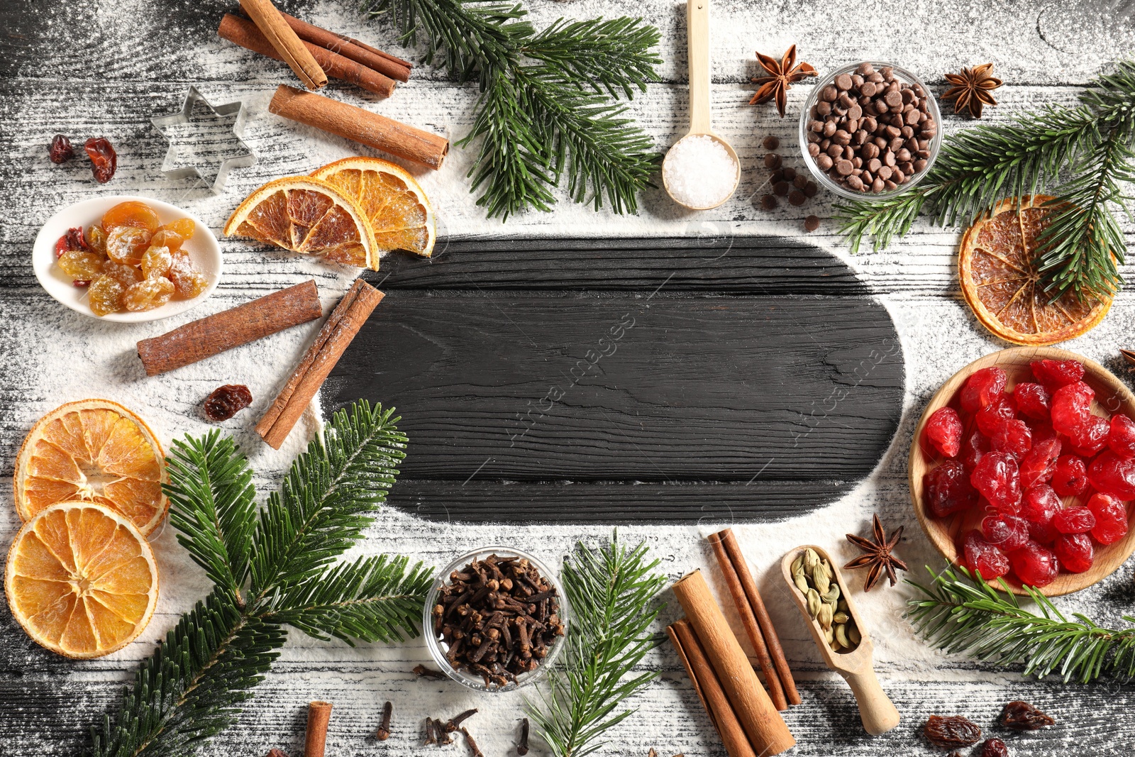 Photo of Frame of different aromatic spices and fir tree branches on black wooden table, flat lay with space for text. Christmas season