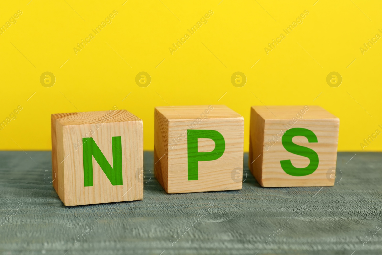 Image of NPS (net promoter score) abbreviation made of cubes on wooden table against yellow background