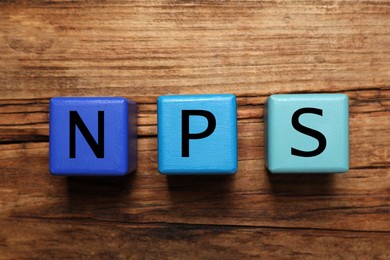 Image of NPS (net promoter score) abbreviation made of cubes on wooden table, top view