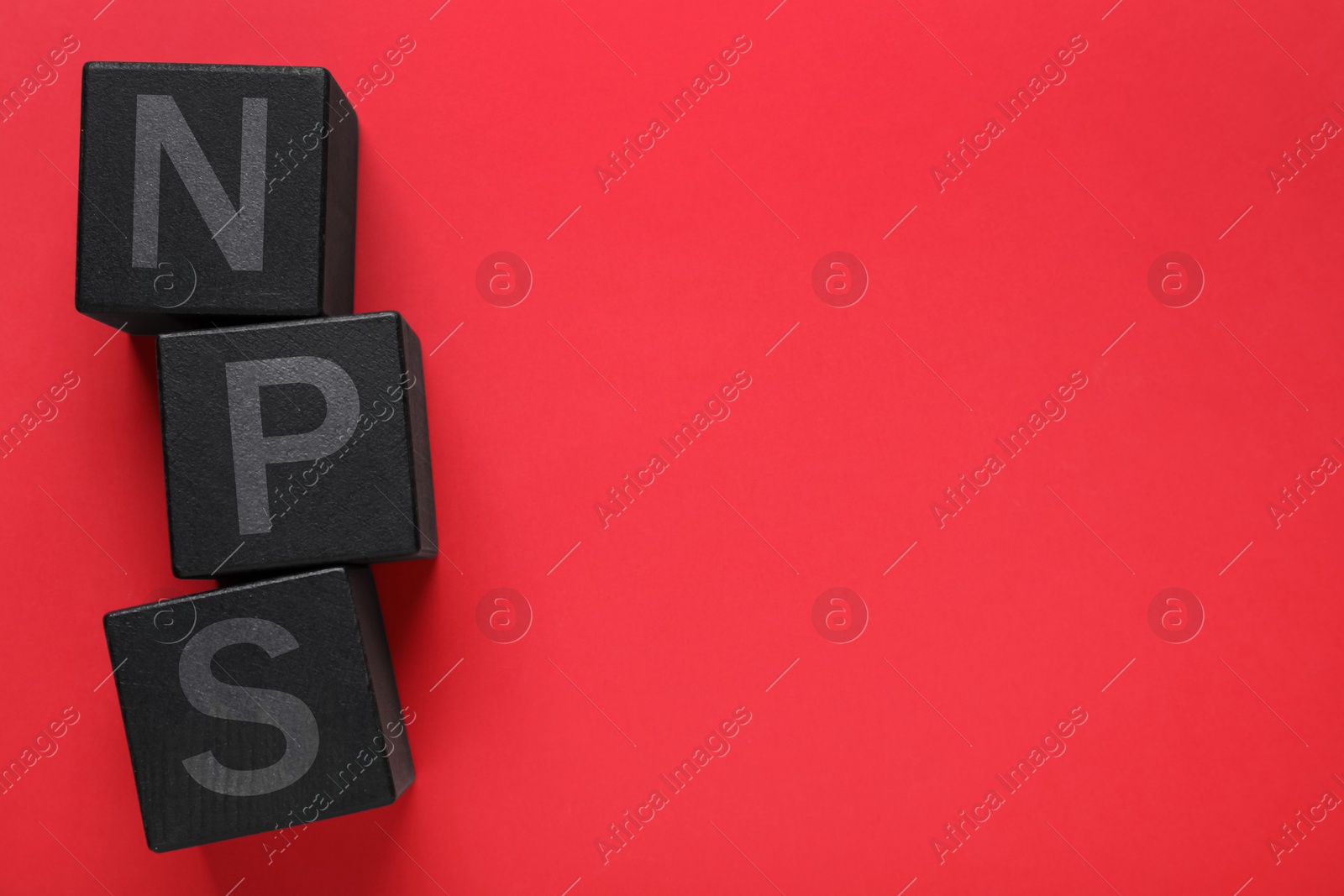 Image of NPS (net promoter score) abbreviation made of black cubes on red background, top view