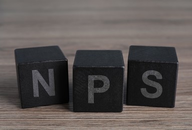 Image of NPS (net promoter score) abbreviation made of black cubes on wooden table