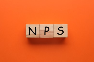 Image of NPS (net promoter score) abbreviation made of wooden cubes on orange background, top view