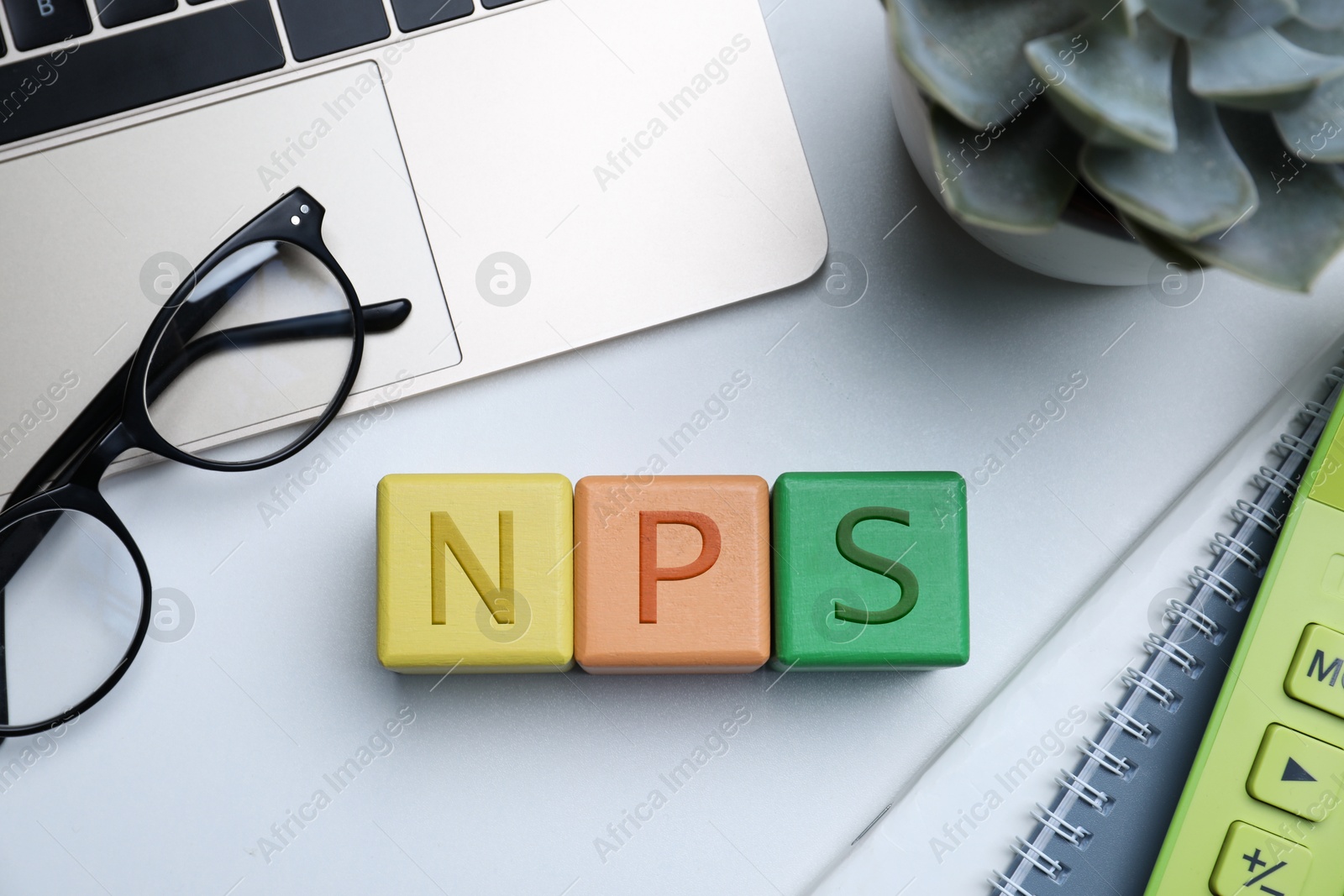 Image of NPS (net promoter score) abbreviation made of cubes, laptop and stationery on grey table, flat lay