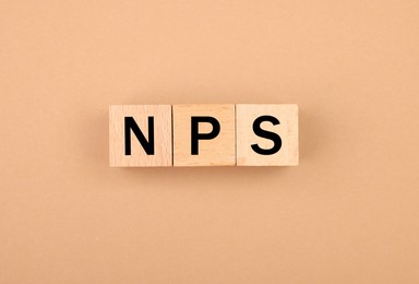 Image of NPS (net promoter score) abbreviation made of wooden cubes on beige background, top view